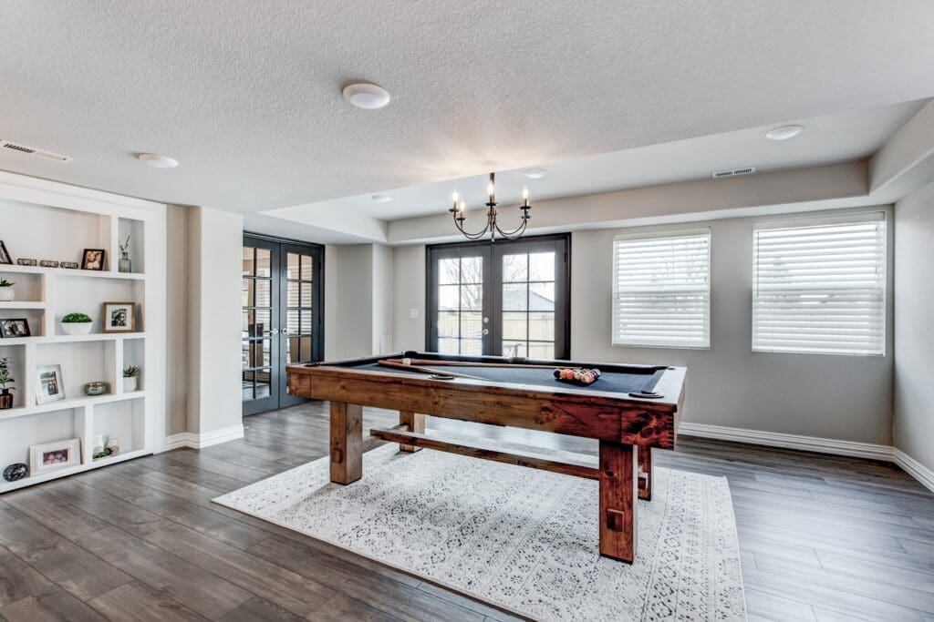 Spacious basement game room with pool table, French doors, and built-in shelving with display decor