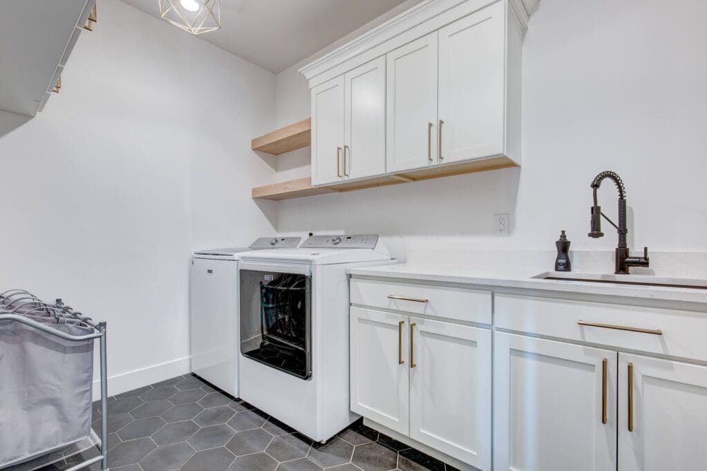 Bright and functional laundry room with white shaker cabinets, black hex tile flooring, and gold hardware