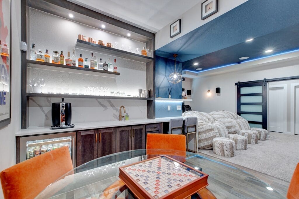 Luxury basement wet bar with floating shelves, backlighting, and a blue-accented lounge space featuring a Scrabble table