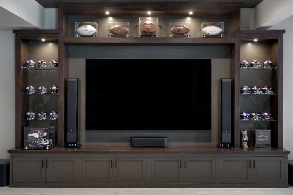 Home theater setup in basement with large dark wood entertainment center, glass shelves, and sports memorabilia display