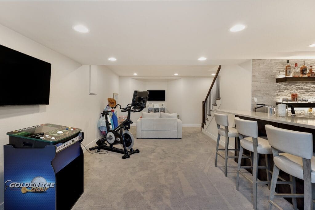 Multifunctional finished basement with fitness equipment, arcade machine, wet bar, and plush media area