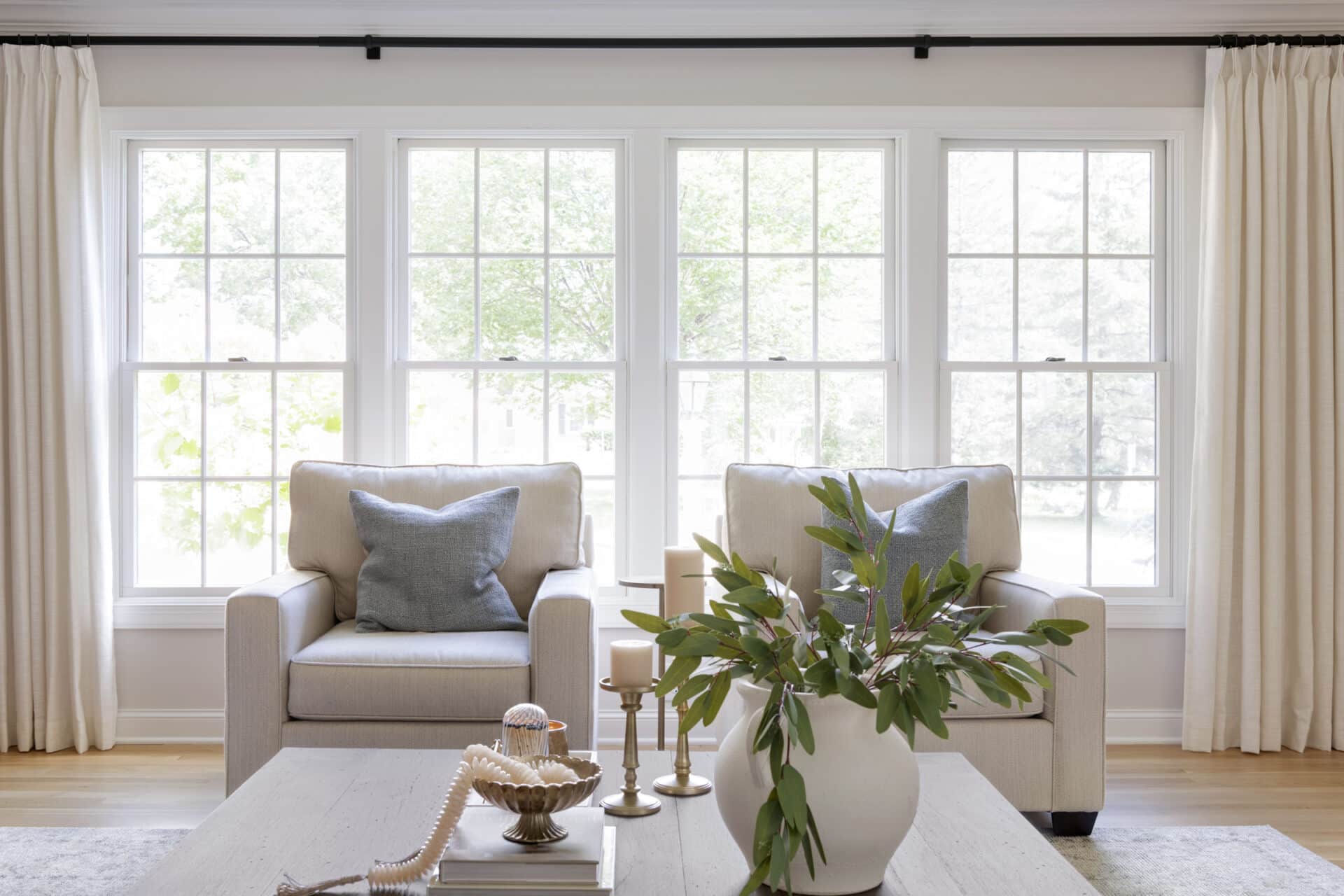 Two upholstered armchairs with blue throw pillows are placed in front of a large window, allowing natural light to fill the soft, neutral-toned living room.