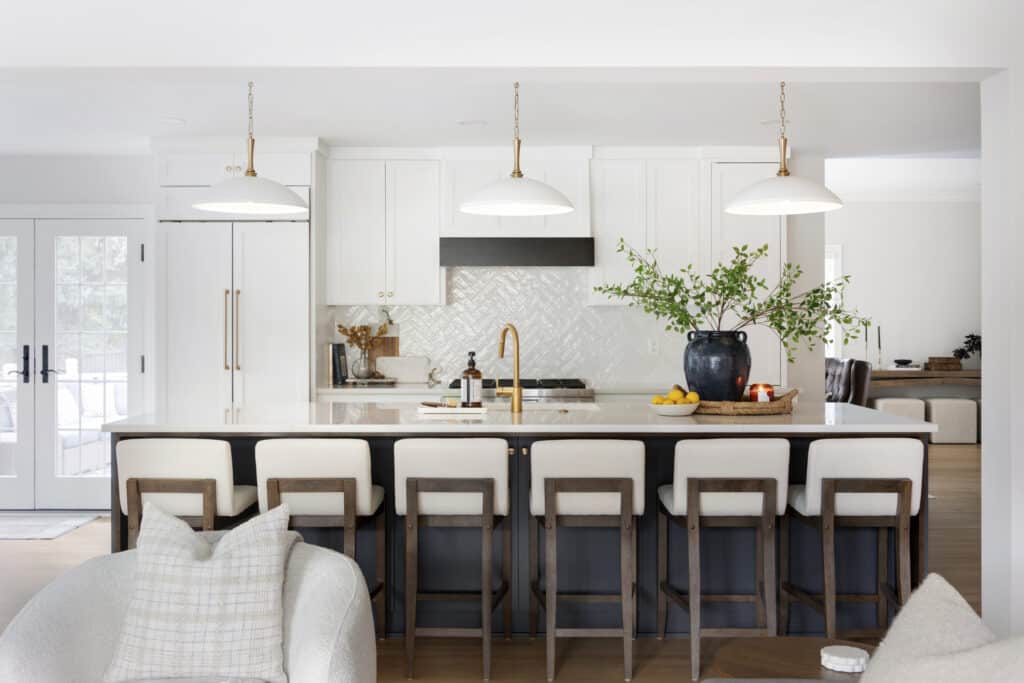 A spacious kitchen with a large center island featuring six barstools, pendant lighting, white cabinetry, and gold hardware, offering both style and function.