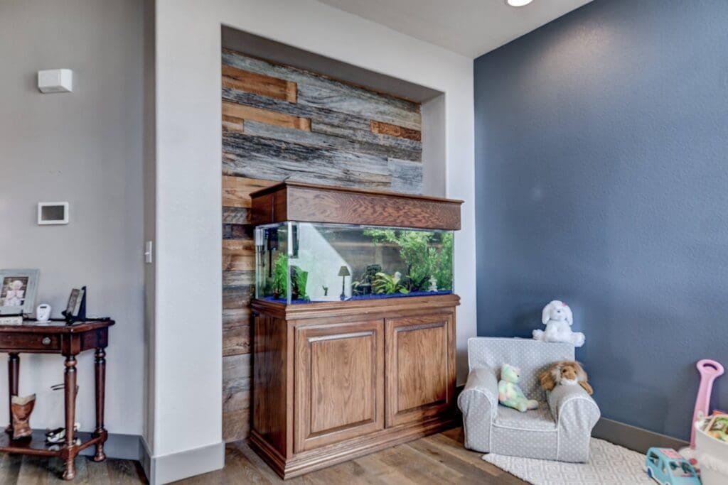 Custom fish tank built into wood-paneled wall next to kids’ play area