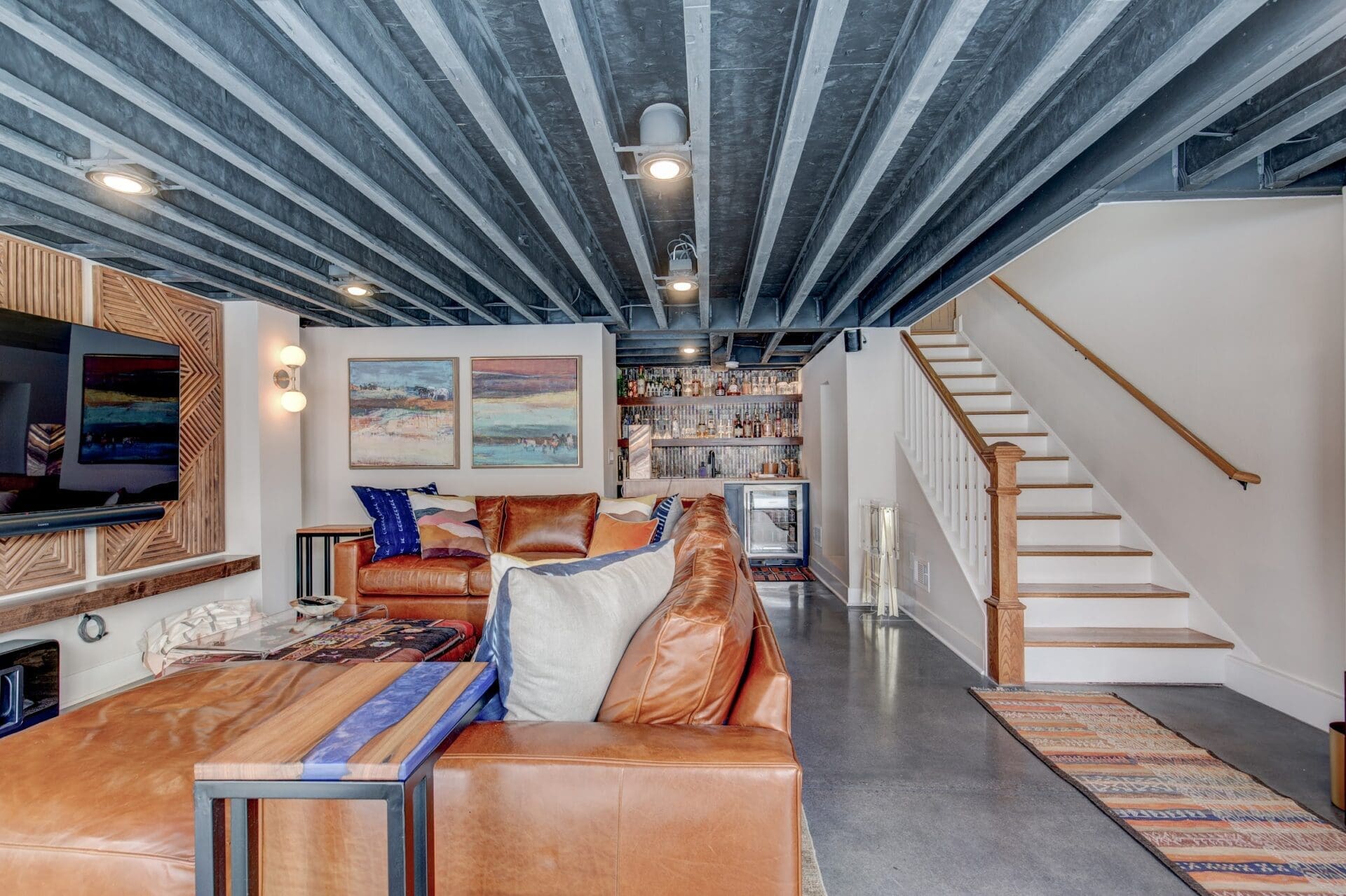 Modern finished basement with exposed beam ceiling, leather sectional, and custom built-in bar in Denver home
