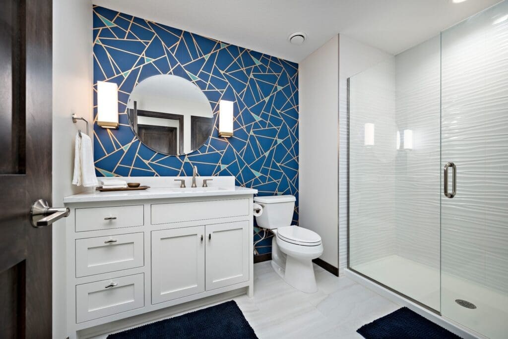 Bold bathroom with geometric blue and gold wallpaper, round mirror, and glass shower enclosure