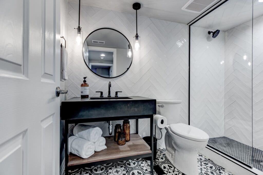 Modern black vanity bathroom with round mirror, pendant lighting, and chevron tile walls