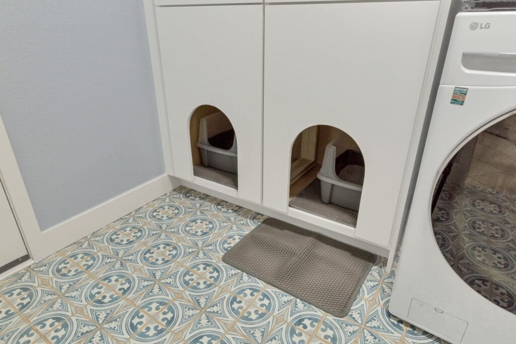 Hidden cat litter cabinet built into laundry room with decorative blue patterned tile