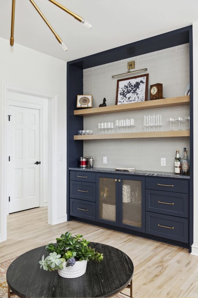 Built-in home bar with navy blue cabinetry, brass hardware, and floating wood shelves