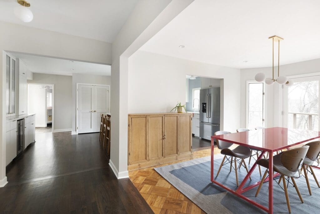 Modern dining room with red table, blue rug, and light wood accents